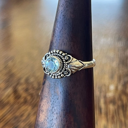 Sterling silver blue topaz detailed ring on wooden cone, angled side view showing Bali-inspired scrollwork, bead edging and leaf detail on band shoulder

