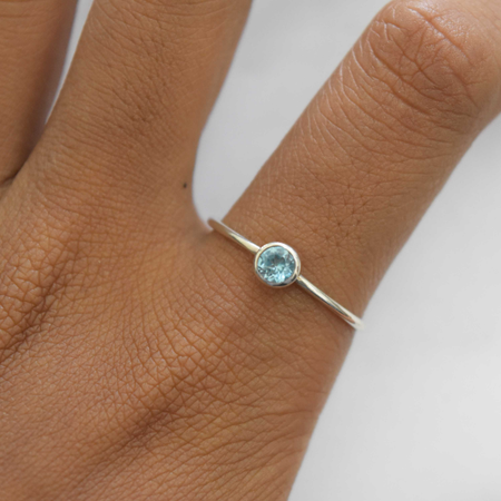 Simple sterling silver blue topaz ring on wooden ring cone, front view showing round-cut pale blue topaz in clean bezel setting on slim hammered band
