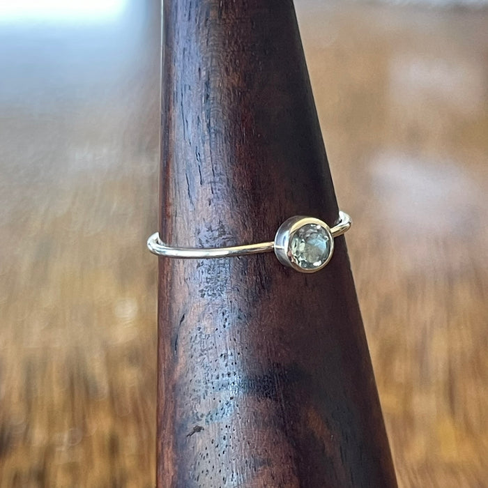 Sterling silver blue topaz ring worn on hand, showing fit and scale of the round-cut aqua blue topaz in simple bezel on slim band

