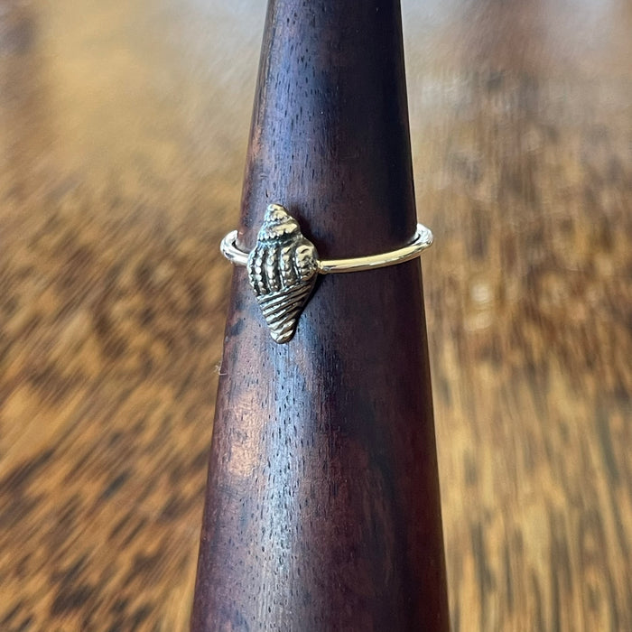 Sterling silver conch shell ring on wooden ring cone, side view showing oxidised shell detail and slim stacking band
