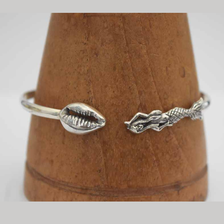 Sterling silver open cuff bangle on wooden cone, showing cowrie shell detail on one end and a detailed mermaid figure on the other
