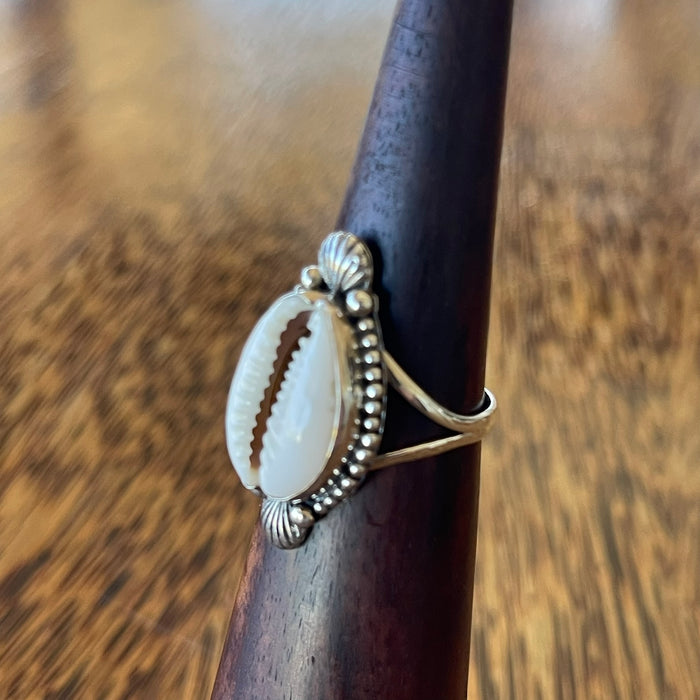 Sterling silver cowrie ring on wooden cone, side angle showing bead edging, scallop shell motifs and slim split band
