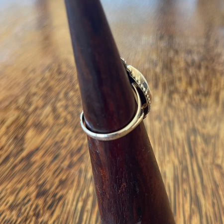 Sterling silver cowrie shell ring on wooden cone, angled side view showing split band and scallop shell detail at base of setting
