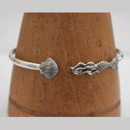 Sterling silver open cuff bangle on wooden cone, showing ridged fan shell detail on one end and a detailed mermaid figure on the other
