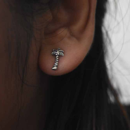 Sterling silver oxidised palm tree stud earring worn on ear, showing detailed frond and twisted trunk design in close-up
