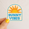 Sunny Vibes retro sunburst vinyl sticker with bold blue lettering and golden sun design — waterproof coastal decal by Daydream Prints
